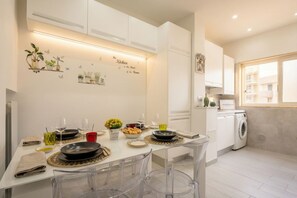 A modern kitchen with white cabinets, a dining table set with plates, glasses, and a vase of flowers.