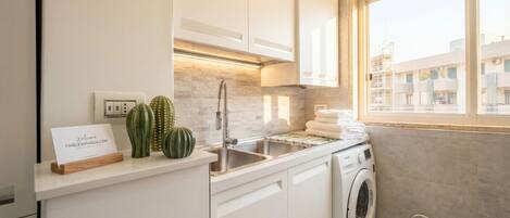 A modern kitchen with a built-in washing machine, a sink, and a window with a view of buildings.