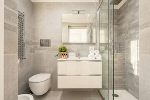 A modern bathroom with a toilet, a glass-enclosed shower, and a vanity with towels.