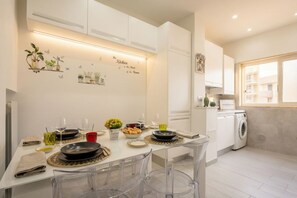 A modern kitchen with white cabinets, a dining table set with plates, glasses, and a vase of flowers.
