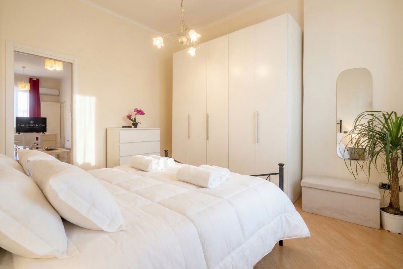 Ein Schlafzimmer mit Bett, Kleiderschrank, Spiegel und einer Zimmerpflanze.