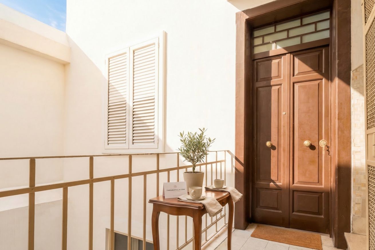A balcony with a wooden railing, a potted plant, a table with a sign, and a brown double door.