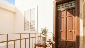 A balcony with a wooden railing, a potted plant, a table with a sign, and a brown double door.