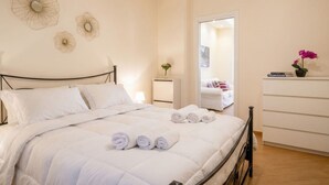 Una cama bien hecha con toallas enrolladas, una mesita de noche con lámpara, un espejo y un aparador con una planta en maceta.