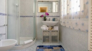Un baño con cabina de ducha de vidrio, lavamanos, espejo y un mueble pequeño con artículos de aseo.