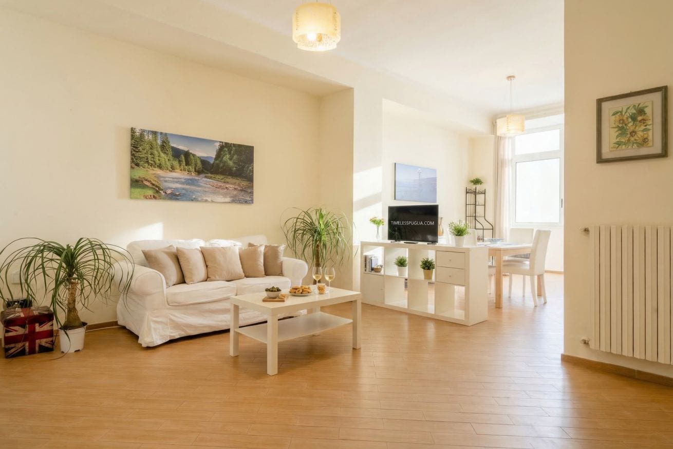 A living room with a white sofa, a coffee table, a TV, and a dining area with a table and chairs.