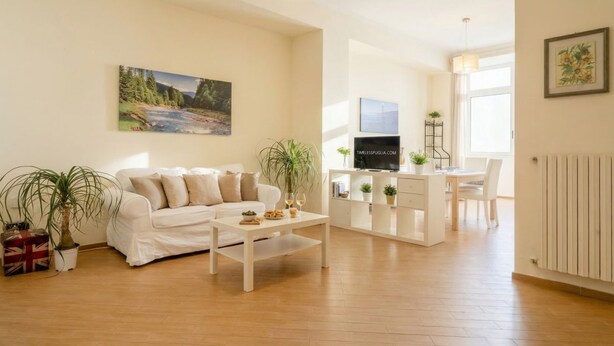 Una sala de estar con un sofá blanco, una mesa de centro, un televisor y un comedor con mesa y sillas.