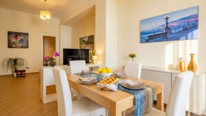 Un comedor con una mesa de madera, sillas blancas, un televisor y obras de arte en las paredes.