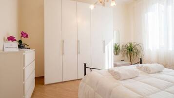 Ein Schlafzimmer mit Bett, Kleiderschrank, Schreibtisch mit Pflanze und Spiegel.