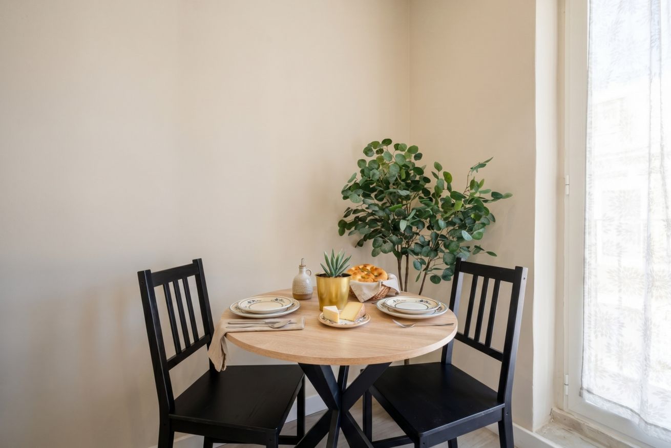 Una mesa de comedor con sillas, una planta y una pequeña disposición de mesa con platos, una jarra y una cesta.