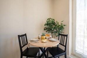 Une table à manger avec des chaises, une plante et une petite table dressée avec des assiettes, un pichet et un panier.