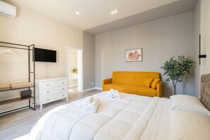 A bedroom with a bed, a yellow sofa, a TV, a dresser, and a plant.