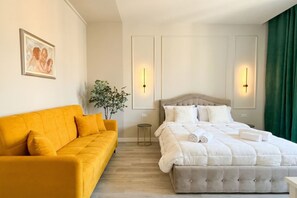 A hotel room with a bed, a sofa, a small plant, and wall-mounted lights.