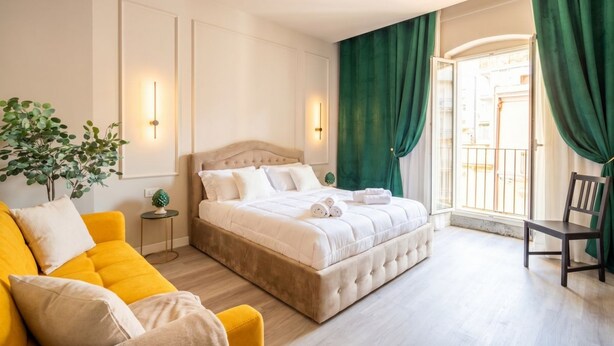 A hotel room with a bed, a yellow sofa, a chair, and a window with curtains. - Alba Suite Apartment (Bari)