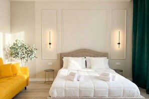 Une chambre à coucher bien rangée, avec un lit, deux tables de chevet, une commode, un canapé jaune et une plante en pot.