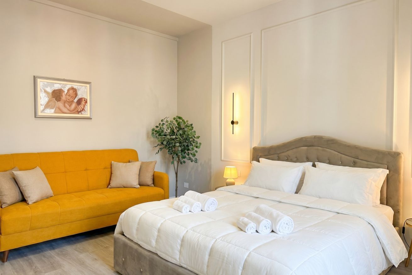 Habitació d'hotel amb un llit, un sofà, una làmpada penjada a la paret i un quadre encimbellat.