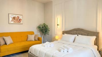 Una camera d'albergo con un letto, una poltrona, una lampada a parete e un quadro incorniciato.