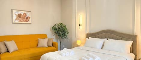 Una habitación de hotel con una cama, un sofá, una lámpara de pared y un cuadro enmarcado.