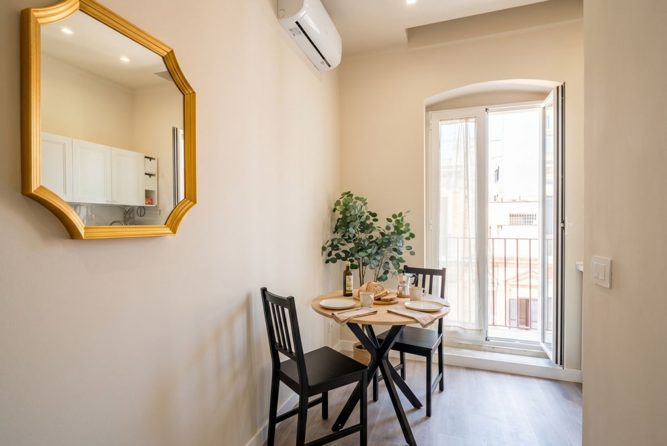 Un coin repas avec une table ronde, des chaises noires, un miroir et une plante en pot.
