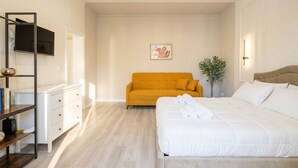 A bedroom with a bed, a sofa, a TV, a plant, and a bookshelf. - Alba Suite Apartment (Bari)