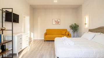 Une chambre à coucher avec un lit, un canapé, une télévision, une plante et une bibliothèque.