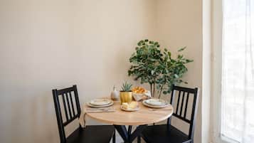 Ein Esstisch mit Stühlen, einer Pflanze und eine kleine Tafel mit Tellern, einer Kanne und einem Korb.