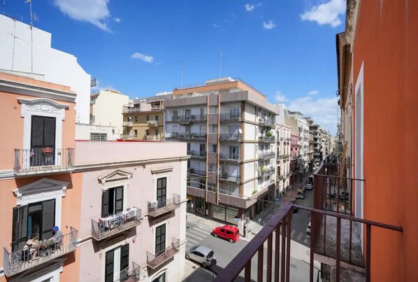 A multi-story urban street with buildings, balconies, and parked cars.