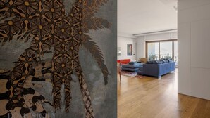 Een moderne woonkamer met een groot abstract kunstwerk aan de muur, een blauwe bank en een houten vloer.