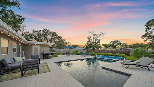 Un patio trasero con piscina, muebles de jardín y una casa.