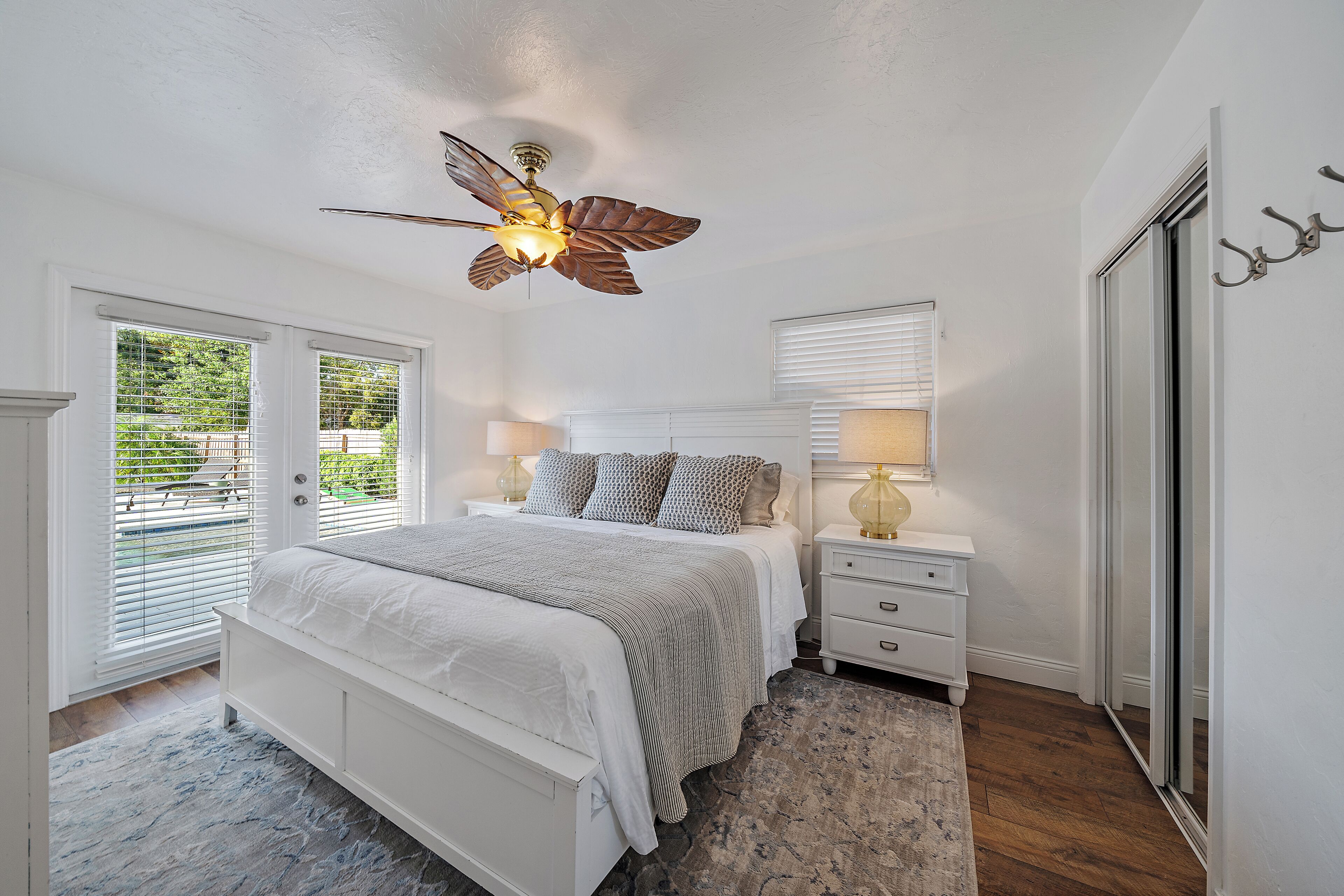 A bedroom with a bed, nightstands, a ceiling fan, and a view through the window.