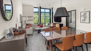 A modern living room with a fireplace, large windows, and a dining area with a glass table and chairs.