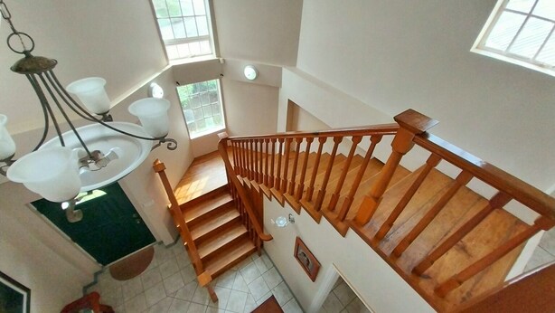 A wooden staircase with a railing, a chandelier, and a window with a view of greenery. - Sérenité. Vigie (Castries)