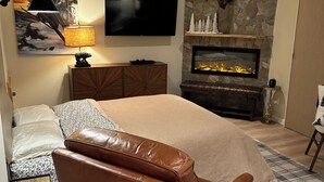 Un dormitorio con una cama grande, televisión, chimenea y una pared de piedra.