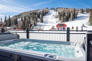 A hot tub with a view of a ski slope and a red bus in the background.
