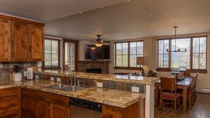 A kitchen with granite countertops, wooden cabinets, a dishwasher, a stone fireplace, and a dining area with a chandelier.