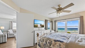 A bedroom with a bed, a ceiling fan, a TV, and a view of the ocean.