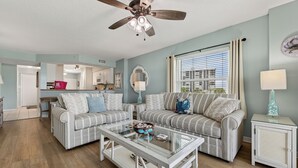 A living room with two striped sofas, a glass coffee table, a ceiling fan, a window with curtains, and a view of the outside.