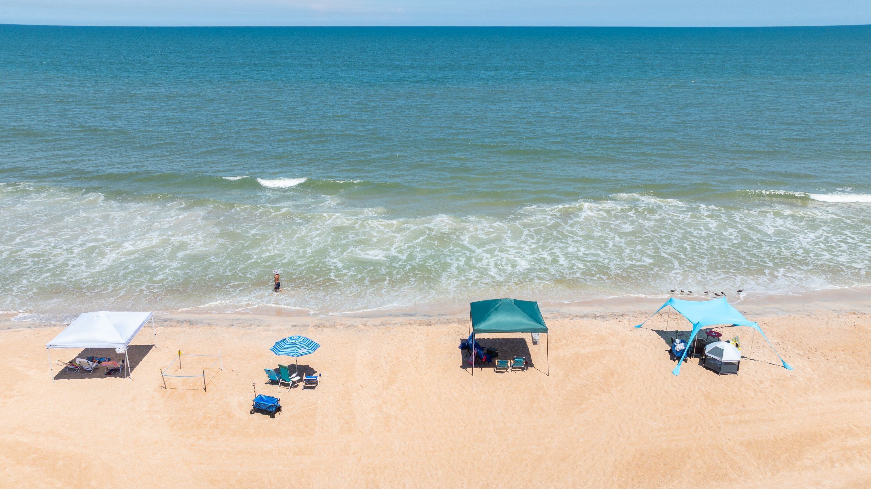 Ein Strand mit Zelt, Sonnensegel und Liegestuhl.