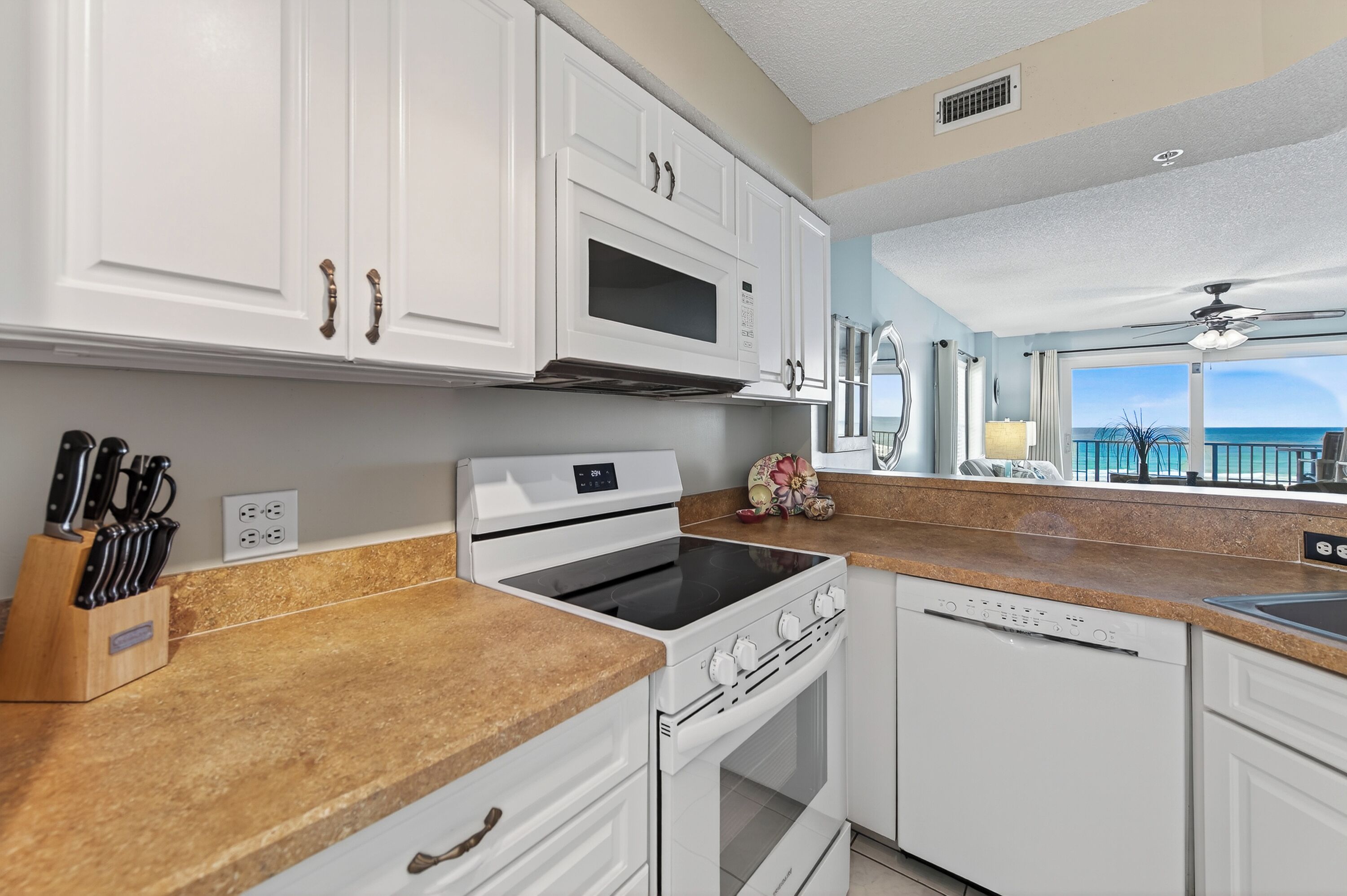 A modern kitchen with white cabinets, a stove, and a dishwasher. There is a window with a view of the ocean.