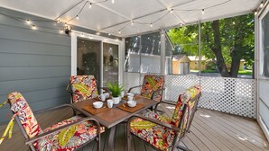 Une terrasse couverte avec une table dressée pour quatre personnes, entourée de chaises colorées, de guirlandes lumineuses et offrant une vue sur l’extérieur.