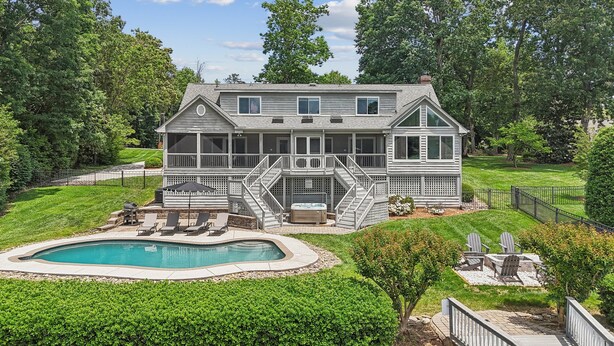 A two-story house with a pool, a hot tub, and a deck with lounge chairs.