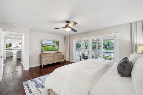 Une chambre avec un grand lit, un ventilateur de plafond, un téléviseur posé sur une commode et une vue sur l’extérieur grâce à une porte-fenêtre coulissante.