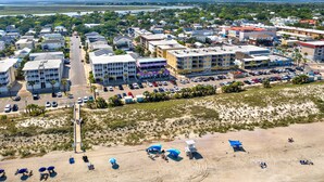 An aerial view of a coastal town with buildings, a beach, and a parking lot.