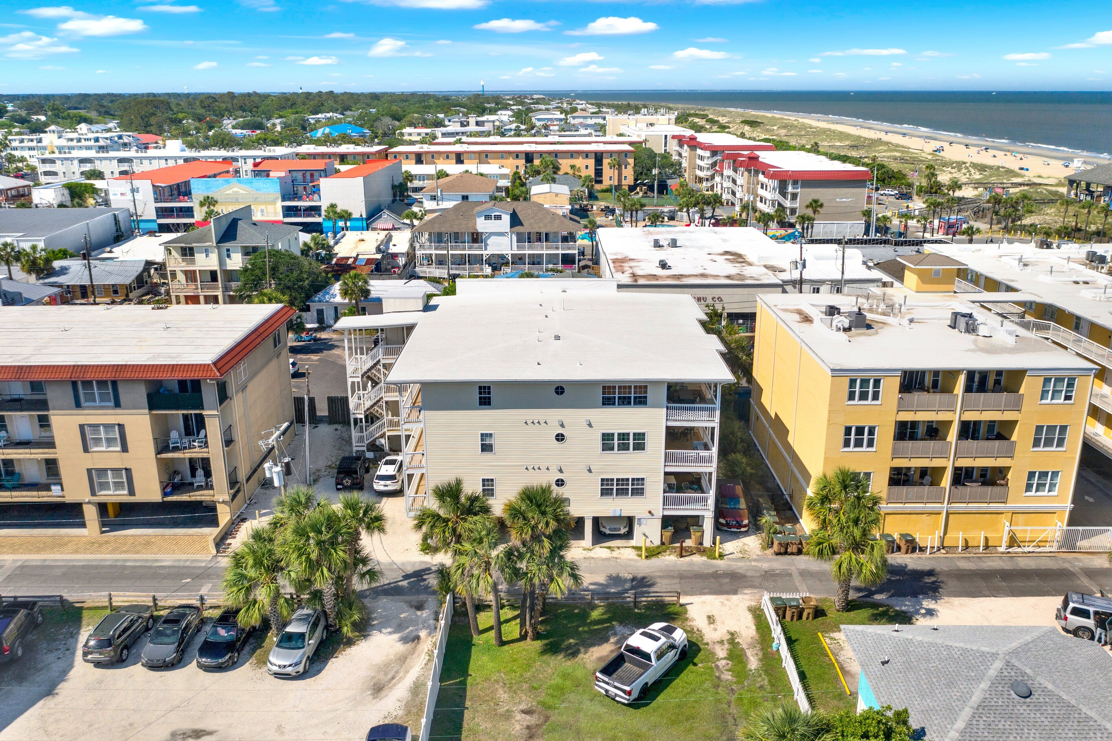 A multi-story hotel with a parking lot, several balconies, and a view of the beach.