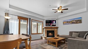 Ein Wohnzimmer mit Kamin, einem darüber montierten Fernseher, einem Deckenventilator und einem Sofa.