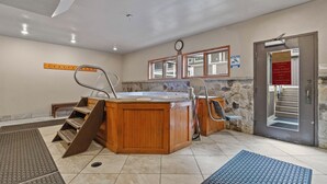 Ein Wellnessbereich mit einer Holzbank, einem Whirlpool und einer Steinwand.