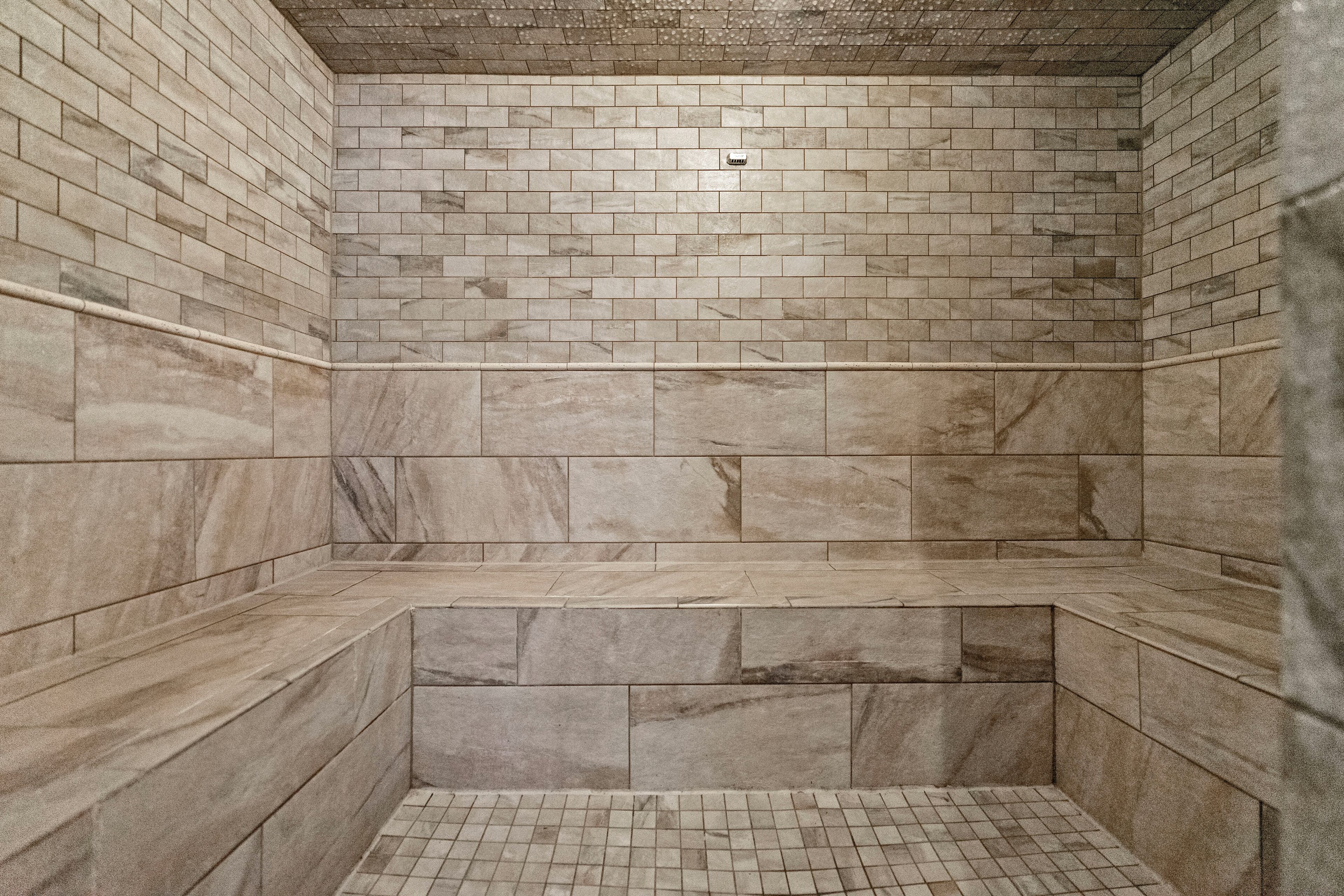 A tiled shower with a marble finish, a built-in bench, and a small overhead light.