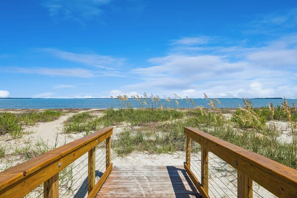 A wooden boardwalk leading to a beach with sand dunes and sea grass. - Serene Beach Home w/ private pool & Tesla Charger – Walk to Port Royal Sound! (Hilton Head Island)