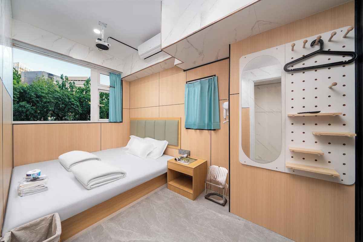 Una habitación de hotel moderna con una cama, una mesita de noche, un espejo, un tendedero en la pared y vistas a zonas verdes.