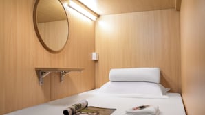 A neatly made bed with white linens, a round mirror, and a small shelf with a magazine. - Windsor Hella Inn (Kowloon)